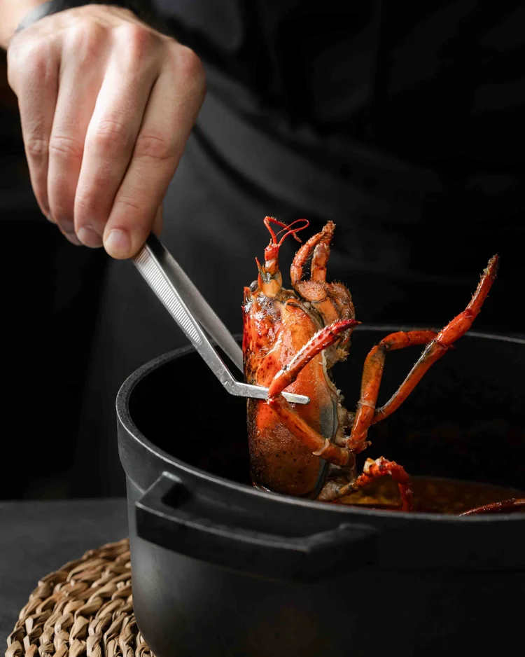 Marisco sostenido con pinzas sobre una olla